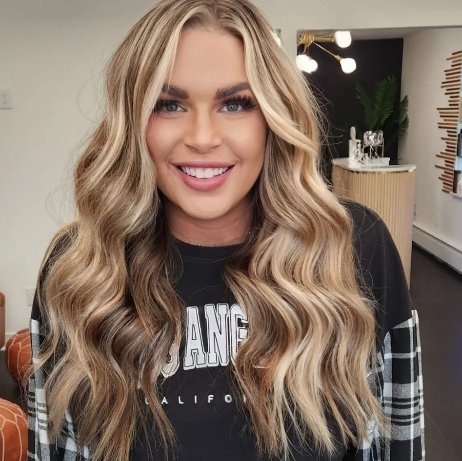 A client smiling after a blonde balayage appointment, her hair curled and finished at the chair.