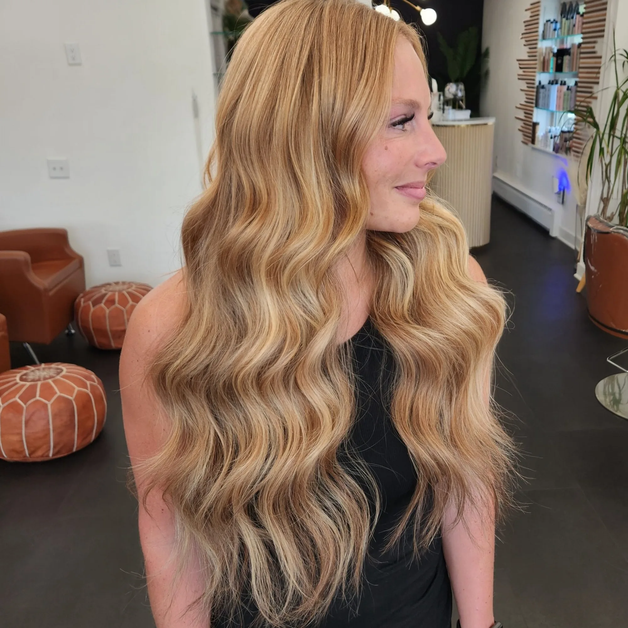 Long blonde beach waves photographed on the salon floor, orange ottomans and mirrors behind.