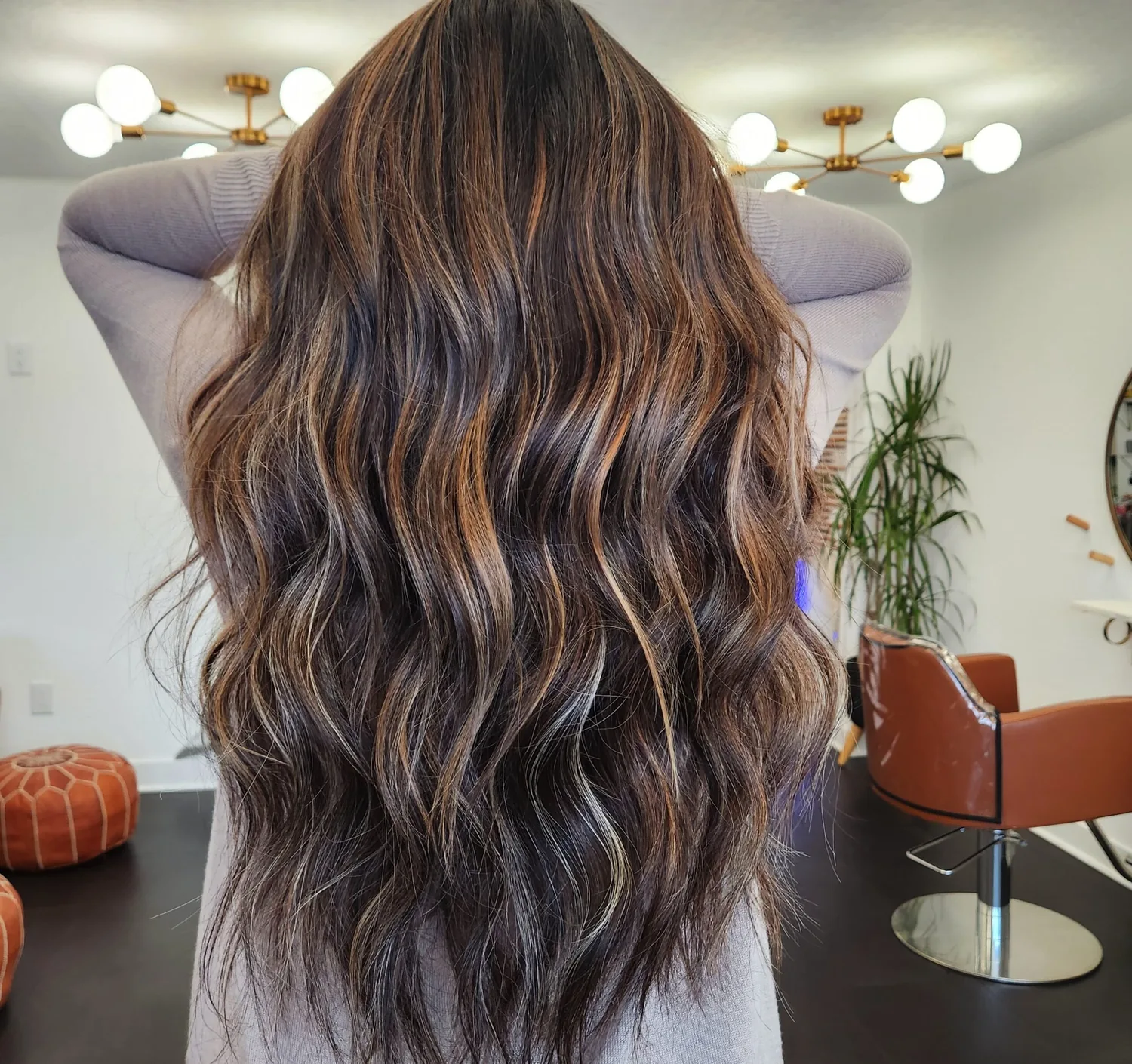 Dimensional brunette balayage seen from behind, warm ribbons of colour running through dark waves.