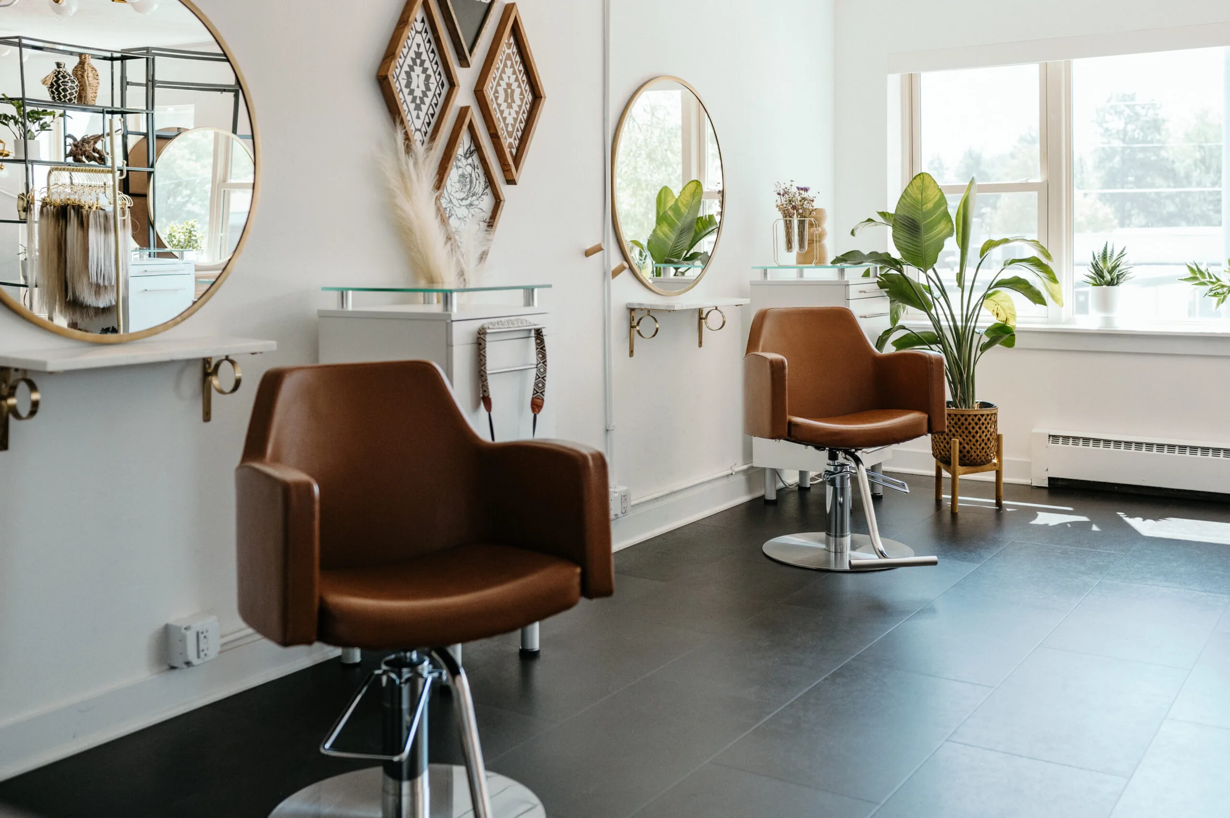 The Hair Garden Salon Suites floor in Middleton: tan leather styling chairs, round mirrors and potted plants along a white wall.