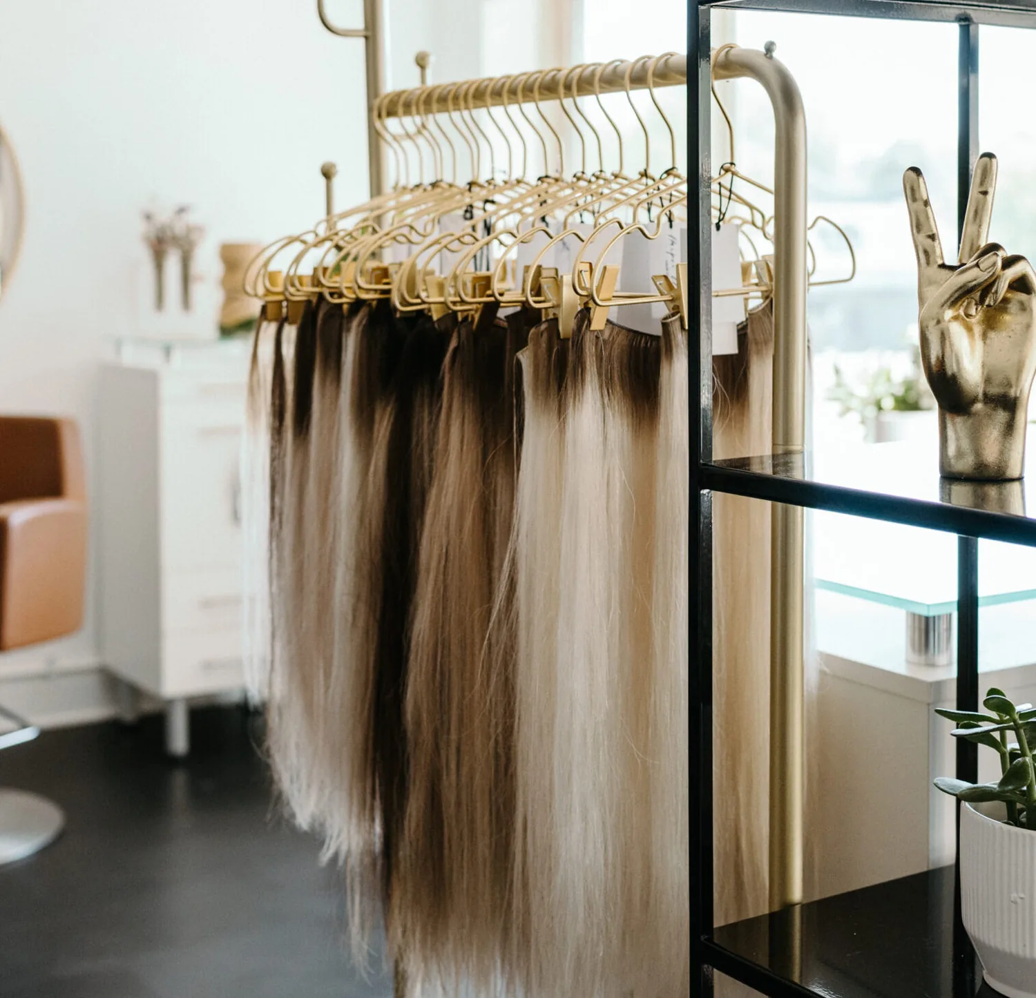 A rack of hand tied extension wefts hanging in graded blonde and brunette shades beside the styling floor.