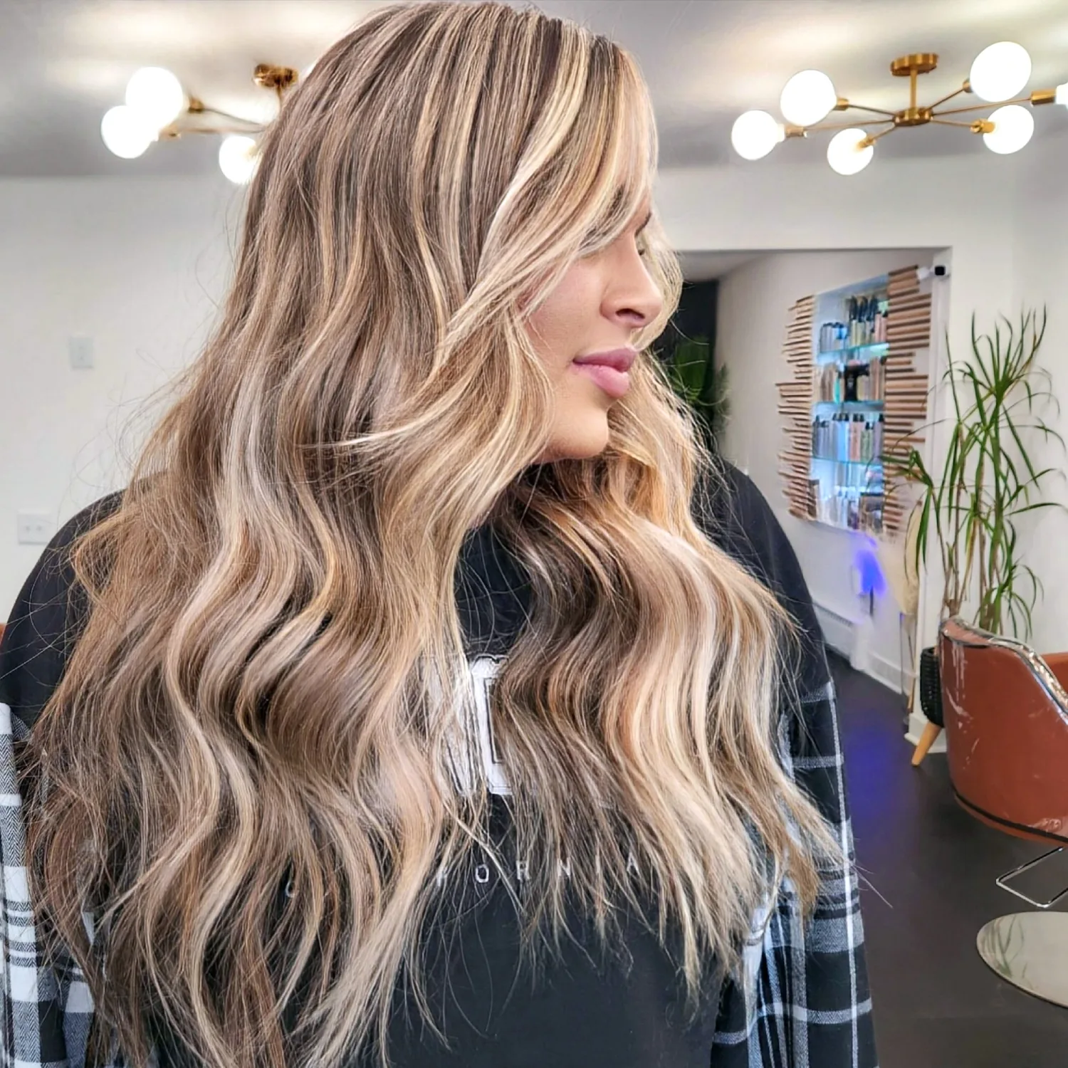 A client in side profile with lived-in blonde balayage falling in loose waves to her waist.