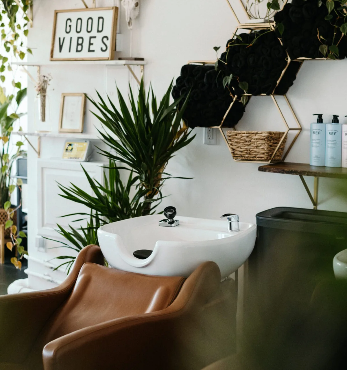 The wash station with a leather chair, trailing plants and a Good Vibes sign on the wall above it.