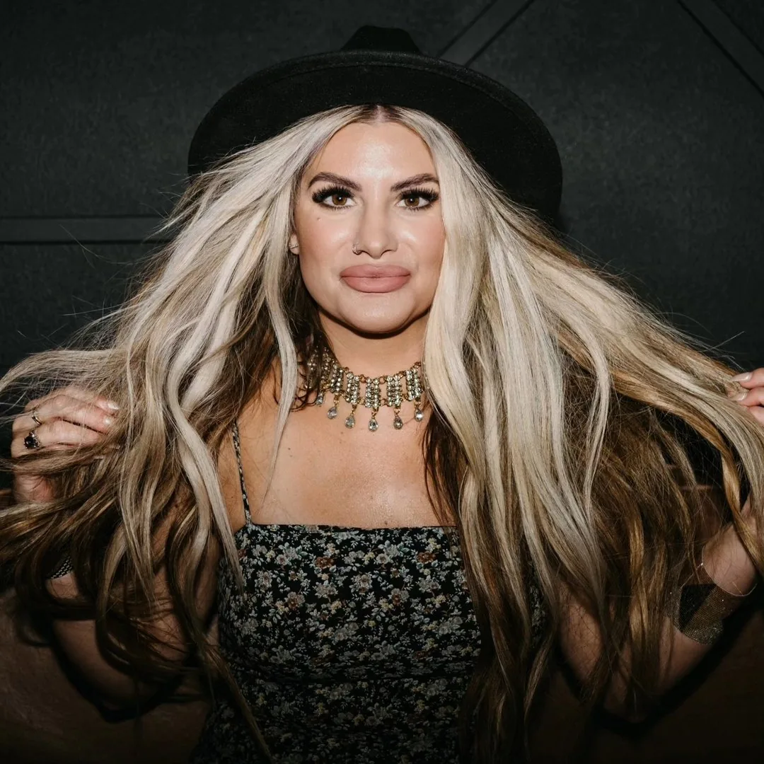 Whitney Wiet in a black hat, her long hand tied extensions falling past her waist in blonde and brunette.